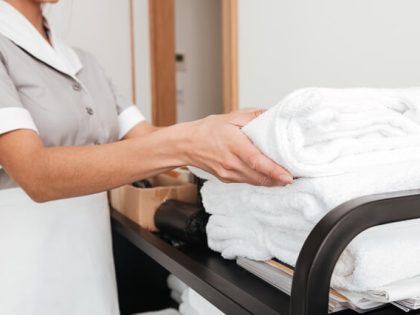 Hotel housekeeper preparing luxury white towels and bed linens for guest room during peak season