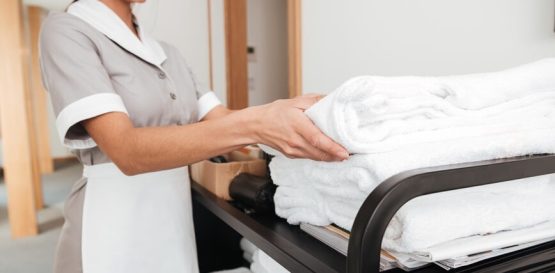 Hotel housekeeper preparing luxury white towels and bed linens for guest room during peak season