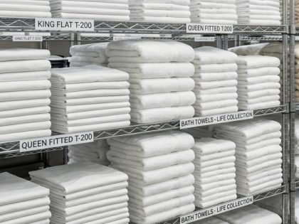 A bright, clean storage room with perfectly folded white towels and sheets stacked on wire shelving.