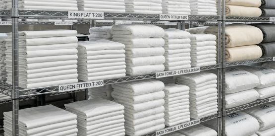 A bright, clean storage room with perfectly folded white towels and sheets stacked on wire shelving.