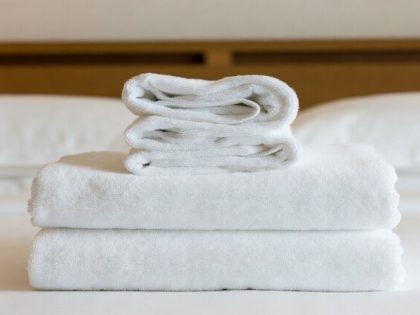 Close-up of a luxurious, fluffy white hotel towel stack on a made bed with soft lighting — conveys premium feel.