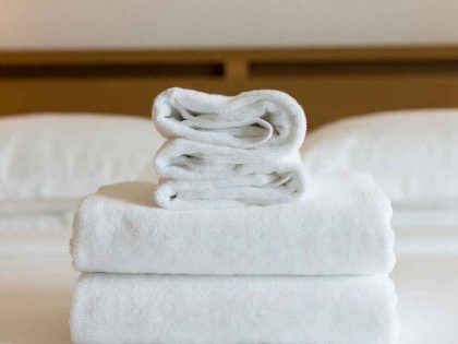 Close-up of a luxurious, fluffy white hotel towel stack on a made bed with soft lighting — conveys premium feel.