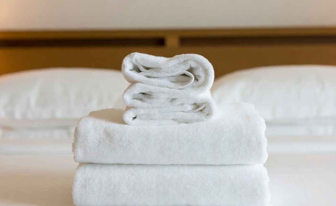 Close-up of a luxurious, fluffy white hotel towel stack on a made bed with soft lighting — conveys premium feel.